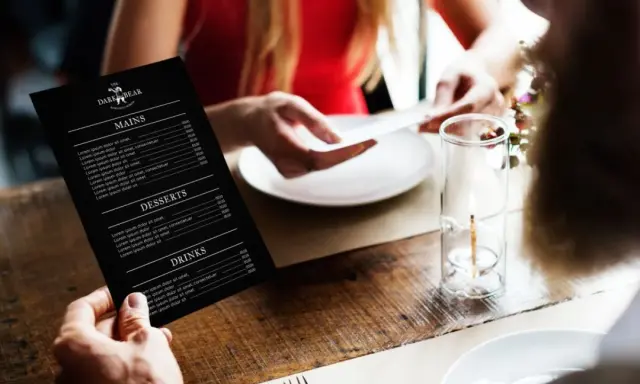 Mężczyzna trzyma czarne menu restauracji "The Dark Bear". Co to jest laminat? To trwałe menu, idealne do restauracji.