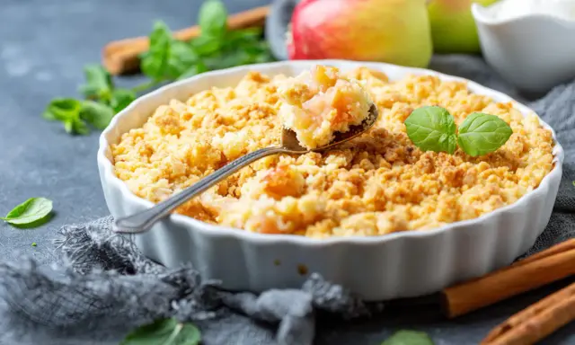 Une cuillère prélève une bouchée dorée de ce meilleur crumble aux pommes, garni de feuilles de menthe fraîche.