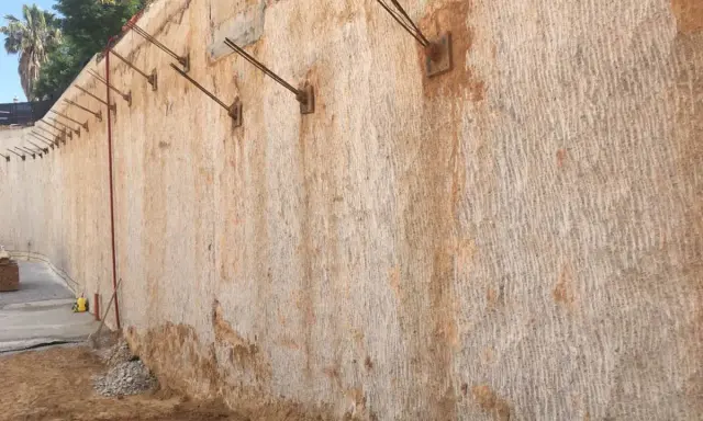 Muros pantalla de contención con anclajes metálicos, mostrando la textura rugosa de la roca y la tierra.