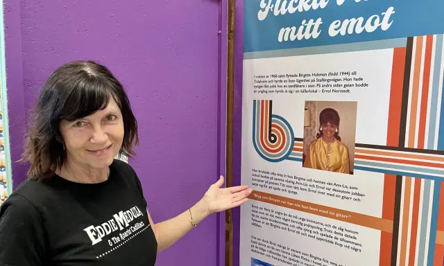 Kvinna i Eddie Meduza-tröja pekar på en utställning om "Flicka i huset mitt emot", en låt av Errol Norstedt.