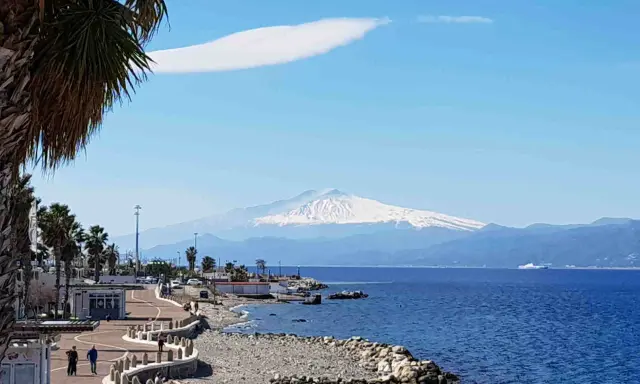 Lungomare di Reggio Calabria con vista sull'Etna innevato. Perfetto per scoprire cosa visitare a Reggio Calabria, tra palme e mare blu.