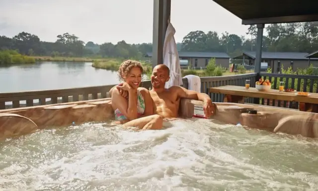 A happy couple enjoys a hot tub with a view of a serene gay lake.