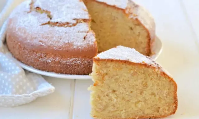 Una fetta di torta di banane soffice, cosparsa di zucchero a velo, accanto alla torta intera su un piatto bianco.