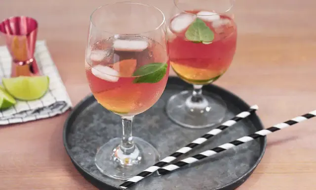Zwei Gläser Rosato Spritz mit Eis und Minze, dazu Limettenspalten und ein Messbecher. Perfekt für einen sommerlichen Genuss.