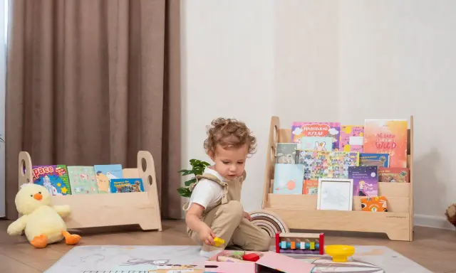 Kleines Kind spielt mit Holzspielzeug vor einem Regal mit Büchern, das eine Sitzordnung im Montessori-Stil widerspiegelt.