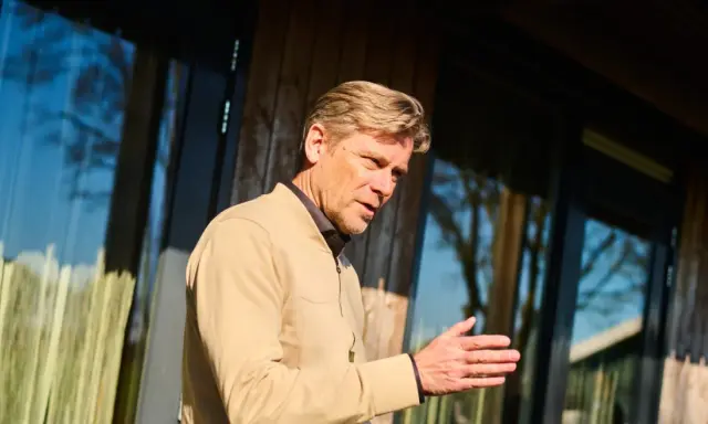 Man met blonde haren, gekleed in een beige jasje, legt met zijn hand uit hoe wordt ik assertiever.