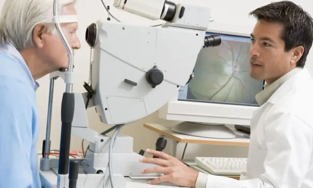 Okulista bada oko pacjenta za pomocą urządzenia. Na ekranie widoczny obraz dna oka, pomocny przy badaniu pachymetria tabela.