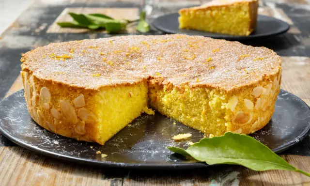 Una deliziosa caprese al limone, cosparsa di zucchero a velo e scorzetta d'arancia, con mandorle sui bordi.