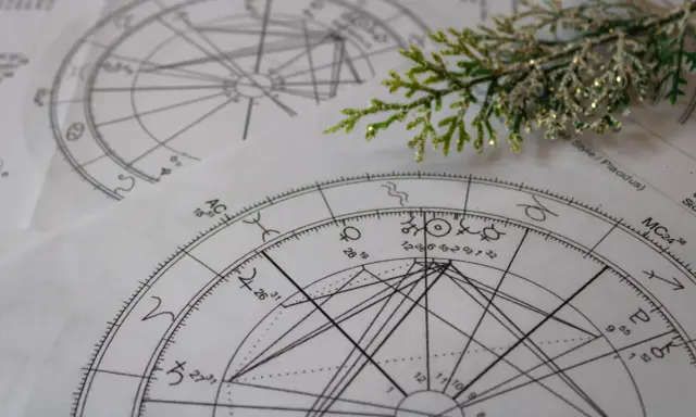 Zrozumienie, jak czytać kosmogram, to klucz do odkrywania tajemnic wszechświata. Na zdjęciu widać fragmenty kosmogramów, symboli astrologicznych i gałązkę iglastą.