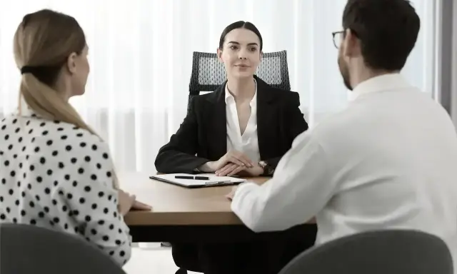 Para omawia z notariuszem podział majątku. Kobieta w kropki i mężczyzna w białej koszuli siedzą naprzeciwko urzędniczki.