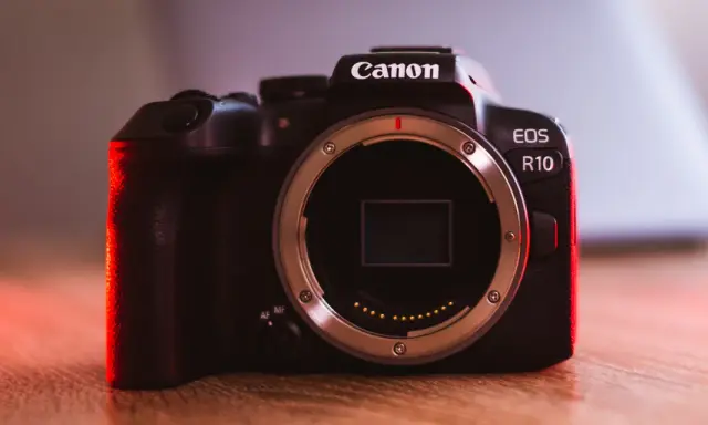 Canon EOS R10 w teście. Ciemna obudowa aparatu z czerwonym podświetleniem, widoczny bagnet obiektywu.