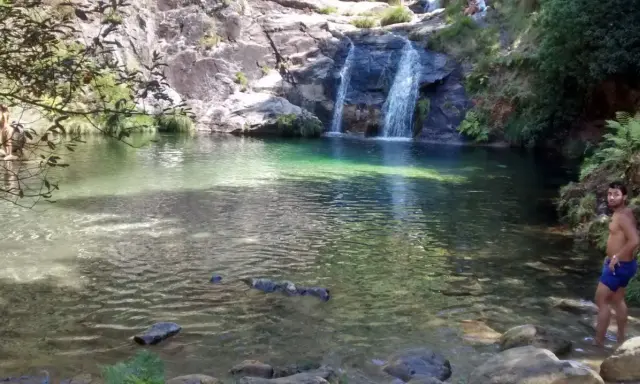 Un hombre disfruta de las pozas de Mougas, con cascadas cayendo sobre rocas y vegetación exuberante.