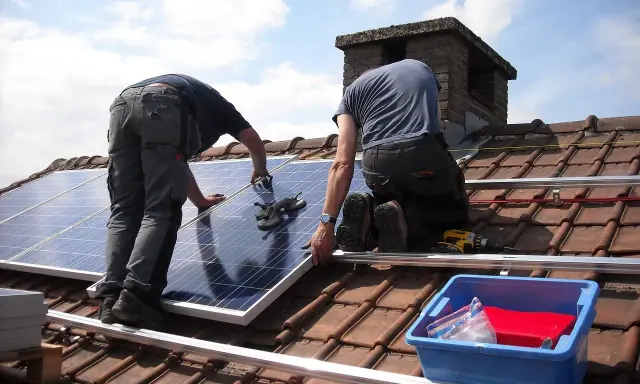 Deux ouvriers installent des panneaux solaires sur un toit. Une demande de travaux panneau solaire est en cours.
