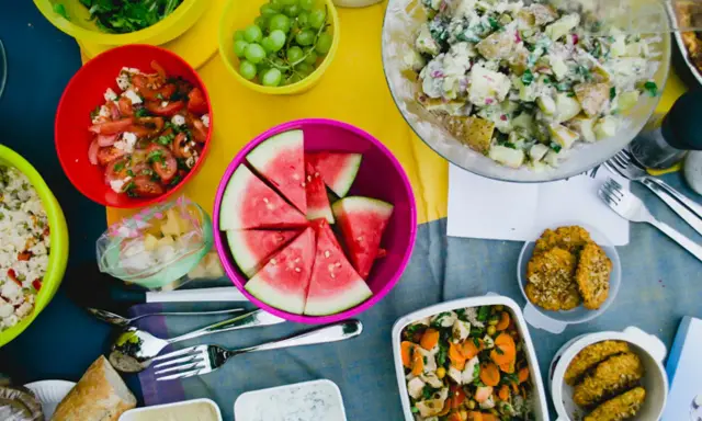 Bunte Schüssel mit Wassermelone, Kartoffelsalat, Trauben und Tomatensalat – leckere Picknick-Snacks für einen sonnigen Tag.