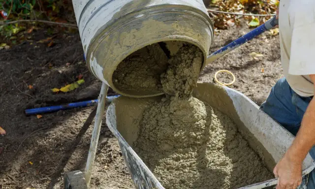 Beton B25 wylewa się z betoniarki do taczki. Proporcje na łopaty są kluczowe dla uzyskania odpowiedniej konsystencji.