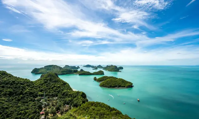 Grüne Inseln ragen aus türkisfarbenem Wasser im Nationalpark Thailand. Kleine Boote gleiten über die ruhige See unter einem blauen Himmel mit weißen Wolken.