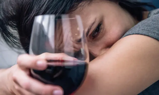 Smutna twarz kobiety z kieliszkiem wina. Czy to jeden z 6 objawów uzależnienia od alkoholu?