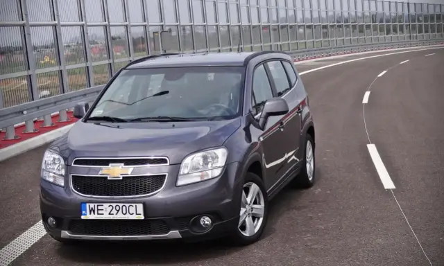 Szary Chevrolet Orlando 1.8 benzyna na pustej drodze, za barierami dźwiękochłonnymi.