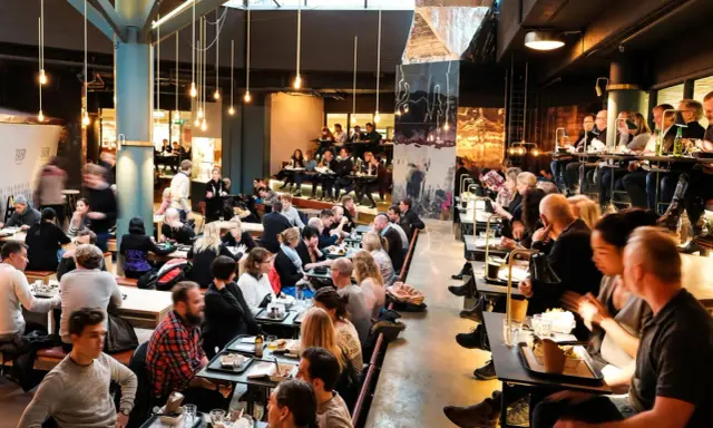 Folk äter och umgås på en livlig **Ringen food court**. Många bord är upptagna, stämningen är social och maten ser god ut.