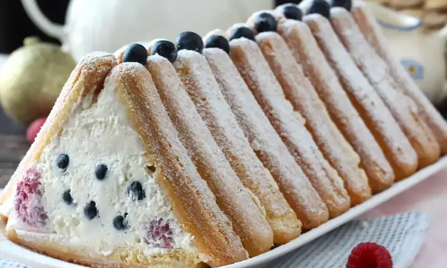 Délicieuse recette buche fruits rouges : un gâteau léger garni de crème et de baies, entouré de biscuits à la cuillère saupoudrés de sucre glace.