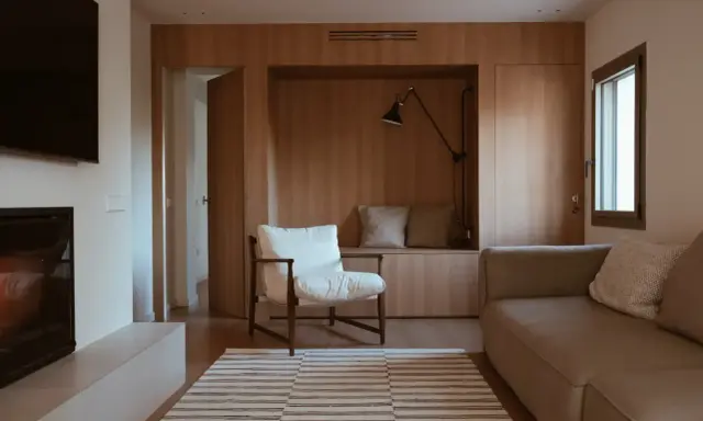 Salones pequeños con mueble de madera integrado, sofá, sillón blanco y alfombra a rayas.