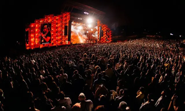 Un enorme pubblico al festival in Portogallo, illuminato da un palco con luci arancioni e un'immagine su schermo.