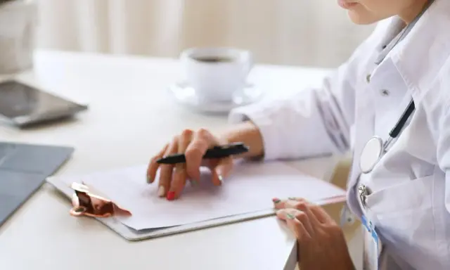 Médica revisa historial para tratamiento de hiperplasia endometrial. En su escritorio, laptop, tablet y café.