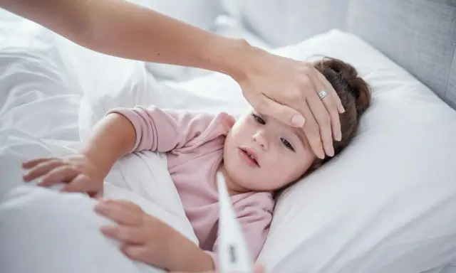 Mama sprawdza temperaturę chorego dziecka, martwiąc się przegrzaniem.