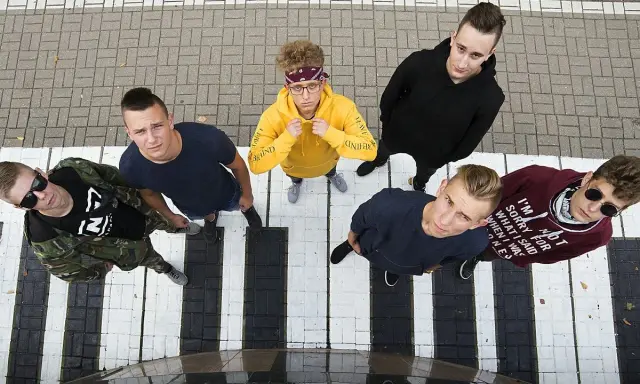 Grupa młodych ludzi, jakby szukających weny raperów, stoi na pasach.