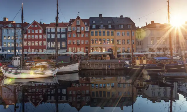 Färgglada hus vid en kanal i Köpenhamn, med båtar i förgrunden. Solen skiner och reflekteras i vattnet. En perfekt vy för en flyg till Köpenhamn-resa.