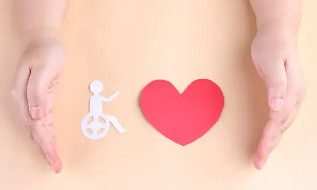 Dwie dłonie obejmują symbol osoby na wózku i serce. Symbolizuje to troskę o osoby z znacznym stopniem niepełnosprawności a alimenty.