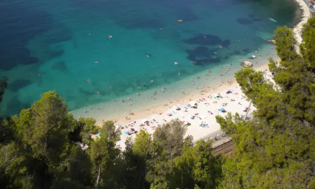 Spiaggia affollata sulla costa azzurra con bambini che giocano in acqua e prendono il sole.