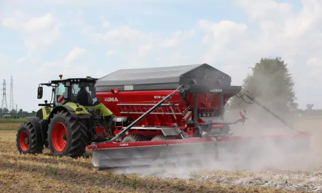 Traktor z rozsiewaczem wapna RCW 1300 marki UNIA na polu. To idealne rozwiązanie, jakie wapno pod warzywa, by zapewnić im najlepsze warunki do wzrostu.