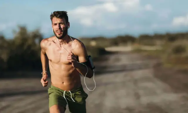 Ein Mann läuft bei Hitze, sein Puls rast. Er trägt Kopfhörer und eine Armbinde für sein Handy.