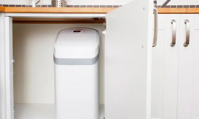 Un adoucisseur d'eau AEG blanc est installé sous un évier de cuisine. C'est une bonne idée de savoir quand installer un adoucisseur d'eau pour une eau plus douce.