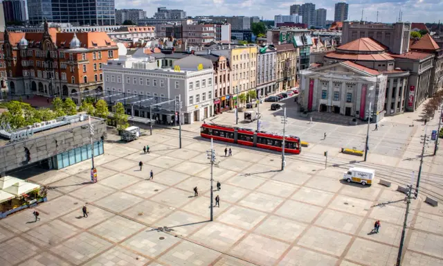 Rynek w Katowicach z czerwonym tramwajem i ludźmi spacerującymi po placu. Idealne miejsce na odkrywanie katowickich atrakcji dla młodzieży.