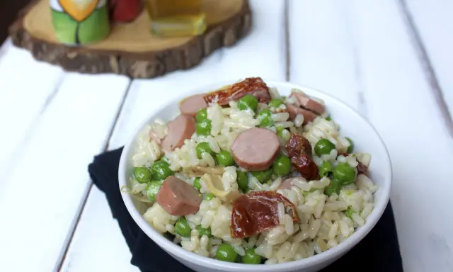 Una ciotola di insalata di riso con piselli, salsiccia e pomodori secchi, pronta per essere gustata.