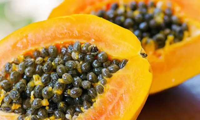 Dwa soczyste kawałki papaya z mnóstwem czarnych nasion w środku.