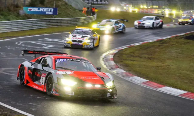 Un Audi R8 rojo y negro compite en las 24 Horas Nürburgring, con otros coches de carreras en la pista mojada.