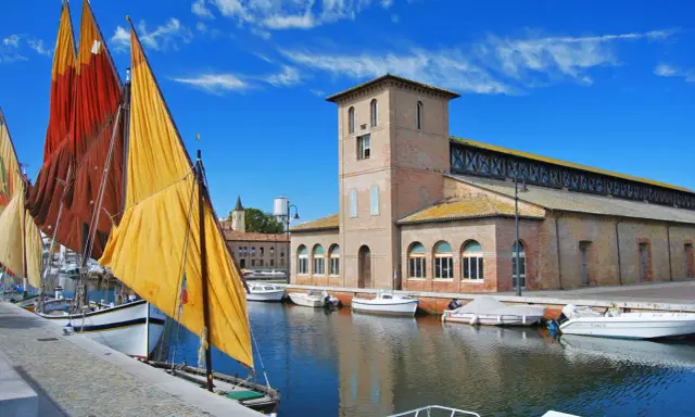 Vele colorate di barche tradizionali ormeggiate nel porto canale di Cervia mare, con l'antico edificio delle saline sullo sfondo.