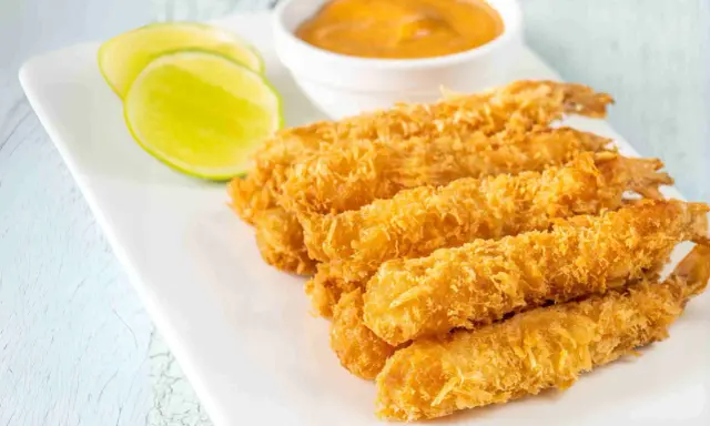 Crujientes gambas a la gabardina doradas, servidas con rodajas de lima y una salsa cremosa.