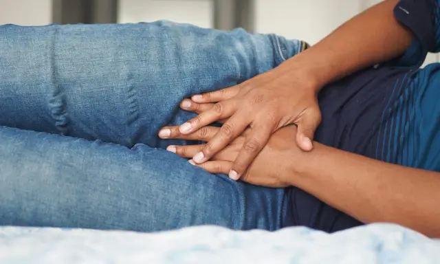 Dłonie na brzuchu w dżinsach. Nietrzymanie moczu może być objawem różnych chorób, np. cukrzycy, problemów z prostatą.
