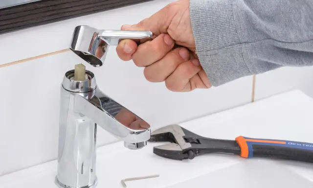 Mano desmontando grifo monomando sin tornillo. Llave inglesa y llave Allen a un lado.