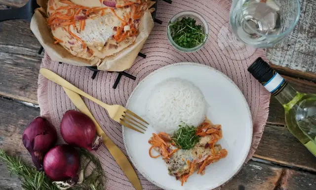 Ein Rotbarschfilet mit Senfsauce, serviert mit Reis und garniert mit Kresse. Dazu passen rote Zwiebeln und ein Glas Weißwein.