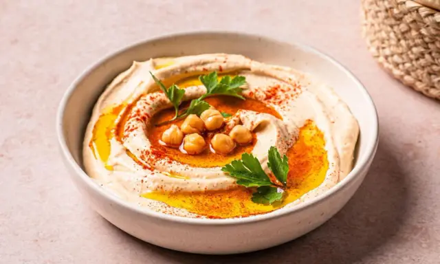 Cremiger Hummus in einer Schüssel, garniert mit Kichererbsen, Petersilie und Paprikapulver. Ein köstliches Gericht mit Hummus, bereit zum Genießen.