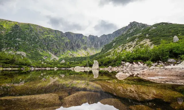 Spokojne, śnieżne stawy odbijają skaliste szczyty i zielone zbocza gór.