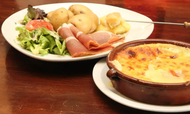 Un plat de spécialité auvergnate : pommes de terre, jambon cru, salade et un gratin de fromage fondant.