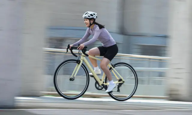 Uśmiechnięta kobieta w kasku pędzi na rowerze, ciesząc się sportami rowerowymi.