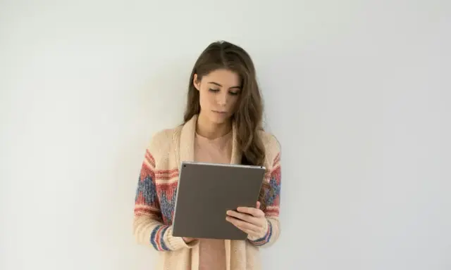 Kobieta w swetrze z wzorem przegląda tablet, być może szukając informacji o długoterminowym zwolnieniu lekarskim.