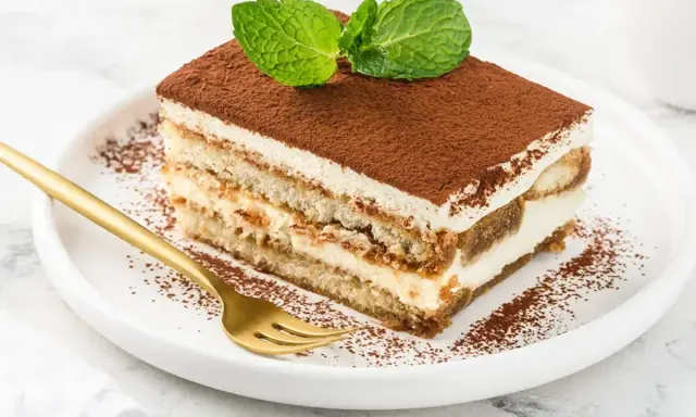 Pyszny kawałek tiramisu z mascarpone, posypany kakao i udekorowany miętą. Idealny na deser.